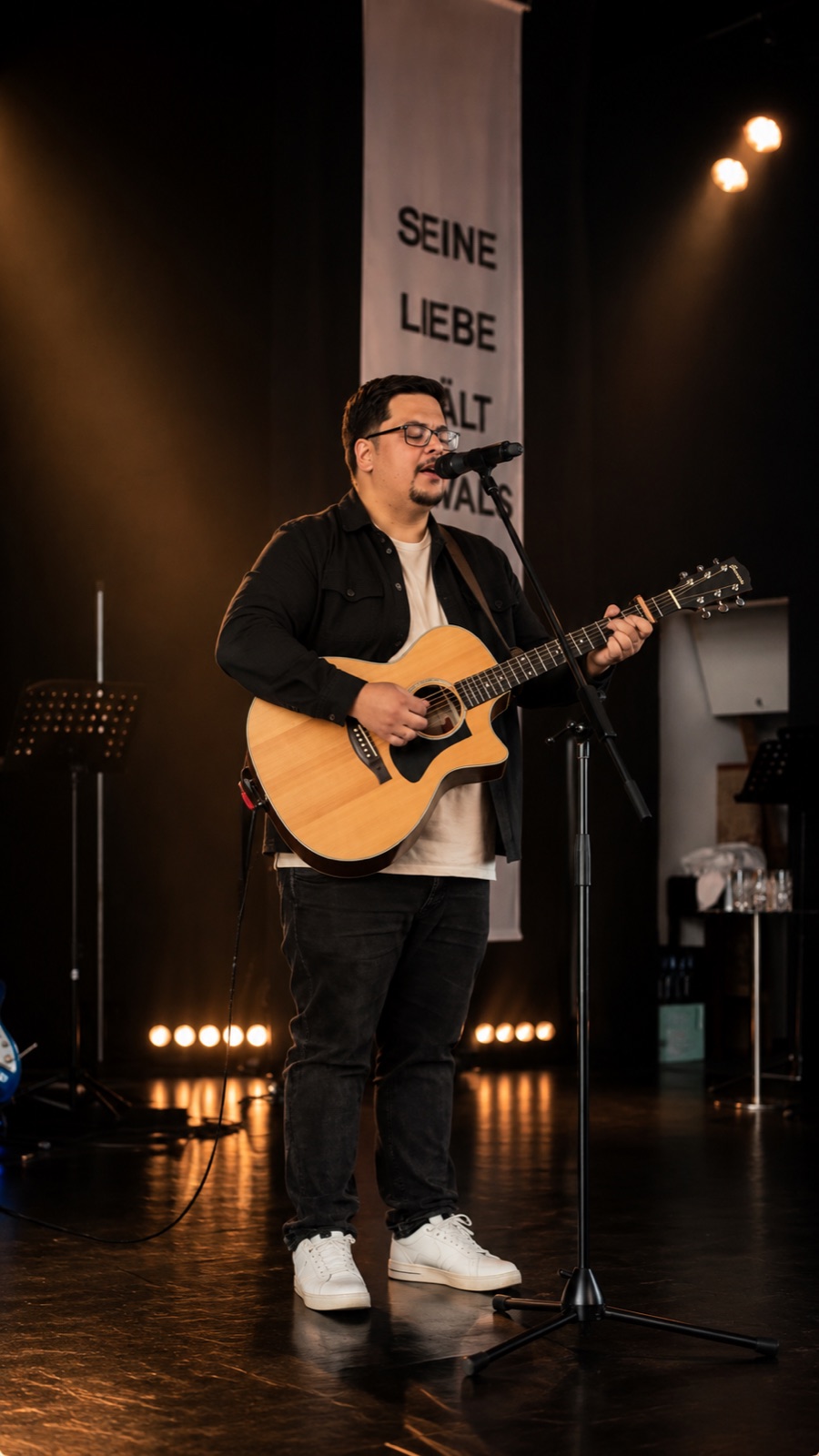 Christian Riesbeck singt mit Gitarre bei einem Bühnenauftritt